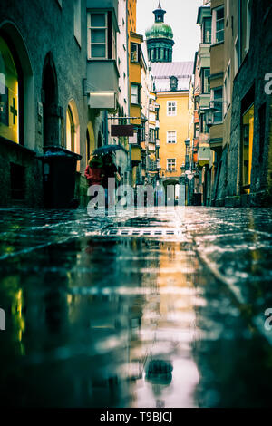 Scène de rue sur jour de pluie à Innsbruck en Autriche avec l'architecture ancienne, des flaques, des réflexions, des parapluies et méconnaissable de personnes Banque D'Images