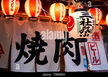 Rideau noren japonais traditionnel à l'entrée d'un restaurant barbecue yakiniku, entouré par des lanternes, dans la soirée, à Asakusa, Tokyo, Japon. Banque D'Images