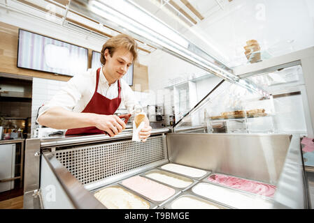 Vendeur de prendre la crème glacée à partir des bacs sur la vitrine et mettre en réfrigérateur le waffle cone dans la pâtisserie, un grand angle de visualisation Banque D'Images