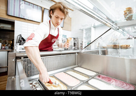 Vendeur de prendre la crème glacée à partir des bacs sur la vitrine et mettre en réfrigérateur le waffle cone dans la pâtisserie, un grand angle de visualisation Banque D'Images