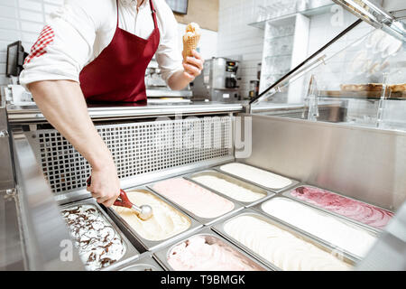Vendeur de prendre la crème glacée à partir des bacs sur la vitrine et mettre en réfrigérateur le waffle cone dans la pâtisserie, un grand angle de visualisation Banque D'Images