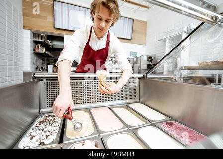 Vendeur de prendre la crème glacée à partir des bacs sur la vitrine et mettre en réfrigérateur le waffle cone dans la pâtisserie, un grand angle de visualisation Banque D'Images