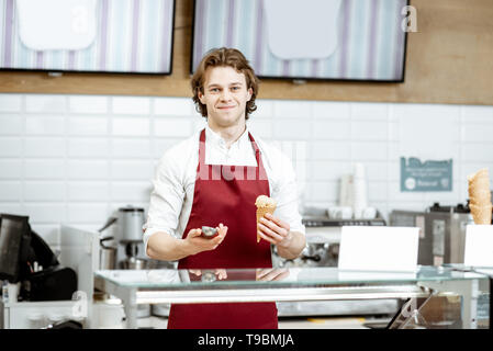 Portrait d'un bel homme en tablier rouge vend de la crème glacée dans la pâtisserie moderne Banque D'Images