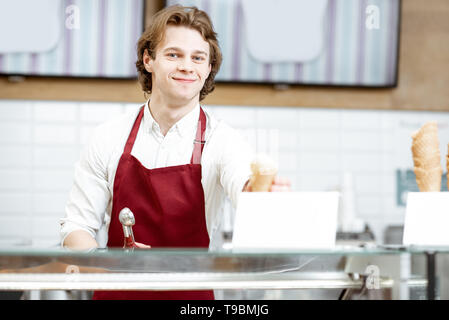 Portrait d'un bel homme en tablier rouge vend de la crème glacée dans la pâtisserie moderne Banque D'Images