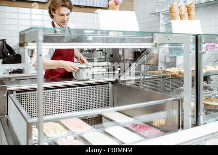 Vendeur mettre plateaux avec crème glacée dans la vitrine réfrigérateur à la pâtisserie Banque D'Images