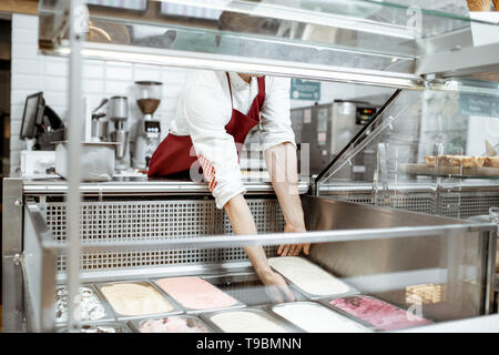 Vendeur mettre plateaux avec crème glacée dans la vitrine réfrigérateur à la pâtisserie Banque D'Images