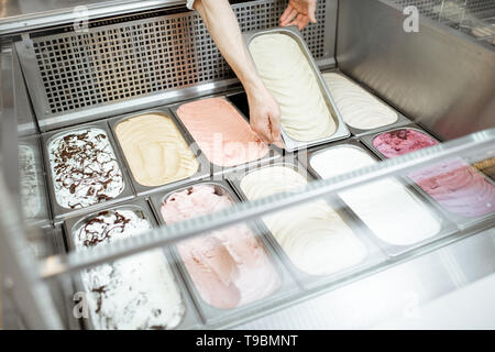Man putting plateaux avec crème glacée dans le réfrigérateur rempli de glace crème avec différentes saveurs dans la boutique Banque D'Images