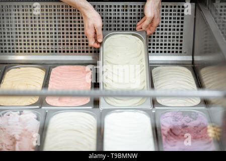 Man putting plateaux avec crème glacée dans le réfrigérateur rempli de glace crème avec différentes saveurs dans la boutique Banque D'Images