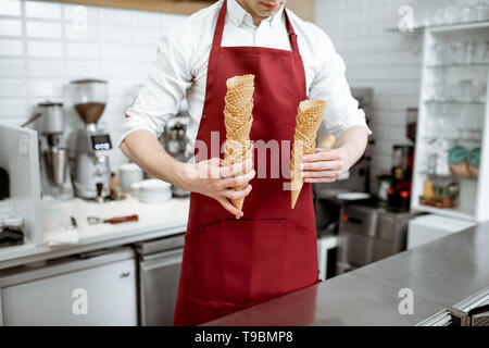 Man in red apron holding cônes alvéolés vend de la crème glacée dans la boutique, close-up view avec pas de visage Banque D'Images