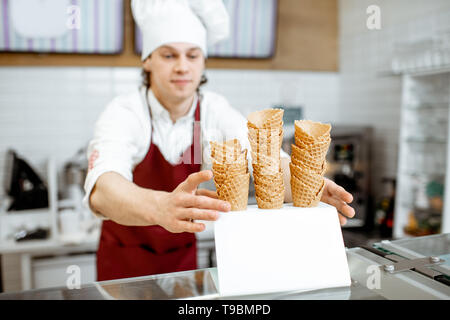 Beau vendeur en tablier et chapeau en tenant les cônes alvéolés tout en glace à la pâtisserie moderne Banque D'Images