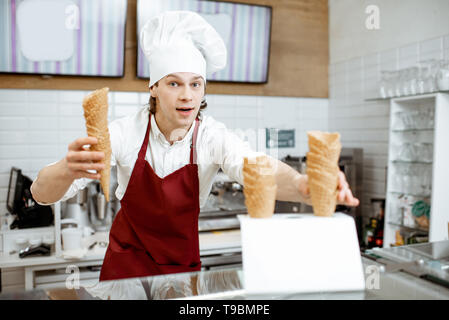Beau vendeur en tablier et chapeau en tenant les cônes alvéolés tout en glace à la pâtisserie moderne Banque D'Images