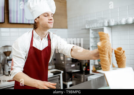 Beau vendeur en tablier et chapeau en tenant les cônes alvéolés tout en glace à la pâtisserie moderne Banque D'Images