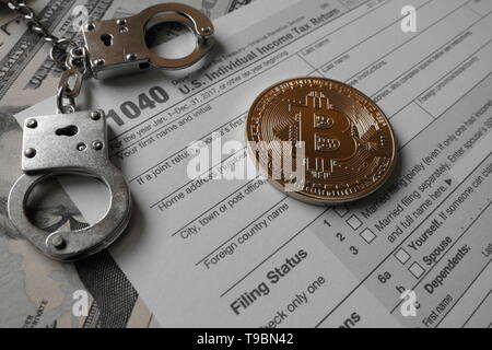 Or une monnaie virtuelle Bitcoin, une monnaie physique en forme, affiché avec des menottes et les États-Unis 1040 formulaire d'impôt, pour l'illustration symbolique taxatio Banque D'Images