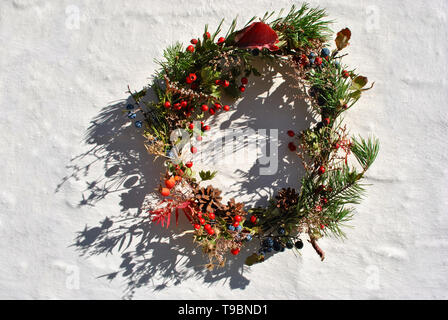 Couronne de Noël avec des baies sauvages (baies d'épine et dog rose baies), de pin avec les cônes secs, les fleurs et les feuilles, la surface du mur blanc Banque D'Images