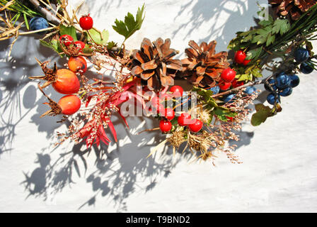 Couronne de Noël avec des baies sauvages (baies d'épine et dog rose baies), de pin avec les cônes secs, les fleurs et les feuilles, la surface du mur blanc, Close up detail Banque D'Images