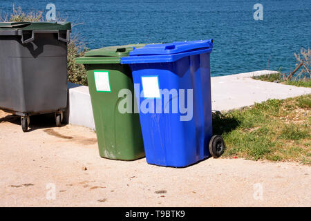 Poubelle, poubelle, bac de recyclage dans le complexe touristique par la mer, le bas-côté de la route qui attendent d'être ramassés par camion poubelle. Conteneurs bleus et verts. Banque D'Images