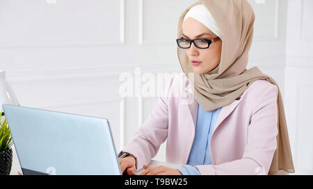Femme musulmane Nerd en beige hijab et costume travaille sur un projet de diplôme Baccalauréat en tapant sur l'ordinateur portable, copy space Banque D'Images