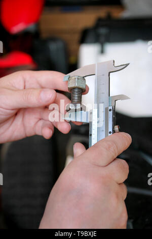 Travailleur avec des outils en mains. Mécanicien est contrôle et mesure de la taille des vis en acier inoxydable avec étrier dans Riga International Motor Show atelier, garage. Banque D'Images