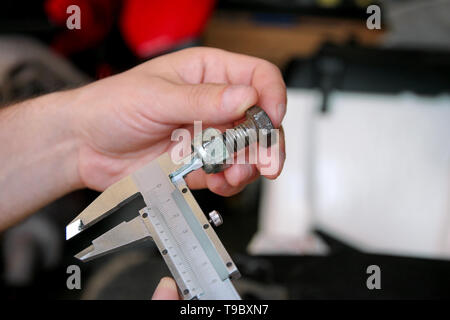 Travailleur avec des outils en mains. Mécanicien est contrôle et mesure de la taille des vis en acier inoxydable avec étrier dans Riga International Motor Show atelier, garage. Banque D'Images