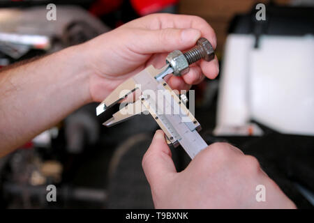 Travailleur avec des outils en mains. Mécanicien est contrôle et mesure de la taille des vis en acier inoxydable avec étrier dans Riga International Motor Show atelier, garage. Banque D'Images