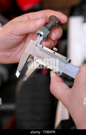 Travailleur avec des outils en mains. Mécanicien est contrôle et mesure de la taille des vis en acier inoxydable avec étrier dans Riga International Motor Show atelier, garage. Banque D'Images