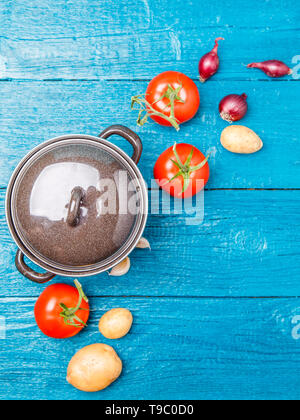 Photo de dessus de pot de fer, tomate, pomme de terre, l'oignon sur fond de bois bleu Banque D'Images