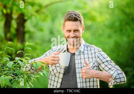 Excellent goût. Profitez de boissons chaudes. Boisson naturelle. Mode de vie sain. Je préfère le thé vert. Boisson rafraîchissante. Plateau barbu homme agriculteur tenir mug fond nature. Plantation de thé vert. Toute la feuille de thé. Banque D'Images