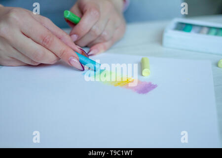 Close-up of female hands sont dessiner avec les craies multicolores sur une feuille blanche, une boîte avec des crayons est à proximité Banque D'Images