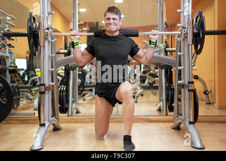 Le sport, le culturisme, le mode de vie et de personnes concept - Young man with barbell squats faire dans une salle de sport . Banque D'Images