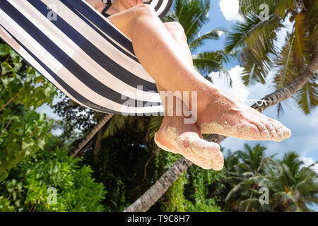 Low Angle View of Sand On Woman's feet Sitting on Hammock At Beach Banque D'Images