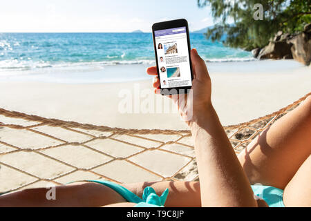 Close-up of a Woman Lying On hamac à l'aide d'application sociale On Mobile Phone At Beach Banque D'Images