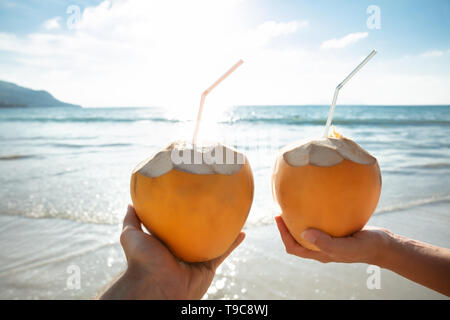 Close-up of Woman's Hand Holding Coconut avec paille en face de la mer idyllique Banque D'Images