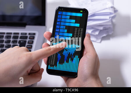 Close-up d'un courtier en bourse à l'aide de téléphone mobile avec le graphique sur écran Banque D'Images