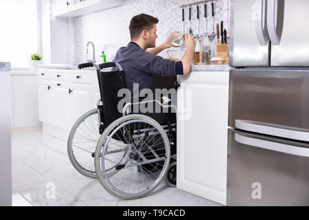 Jeune homme handicapé assis sur fauteuil Preparing Food In Kitchen Banque D'Images