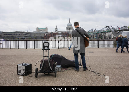 Un homme musicien ambulant à jouer de la guitare en face de la Tate Modern avec vue sur la Cathédrale St Paul, London, UK Banque D'Images