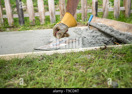 Low angle vue rapprochée d'un homme à l'aide de gants de mise à niveau de la surface d'une plaque de béton à l'extérieur en cour avant ou arrière. Banque D'Images