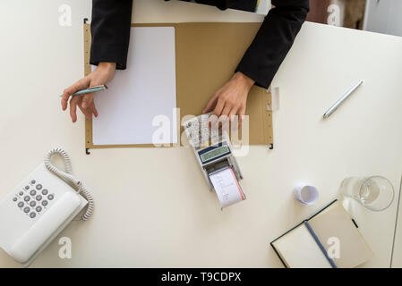 Vue supérieure de l'homme d'affaires à l'aide d'une calculatrice sur un bureau avec du papier vierge. Banque D'Images