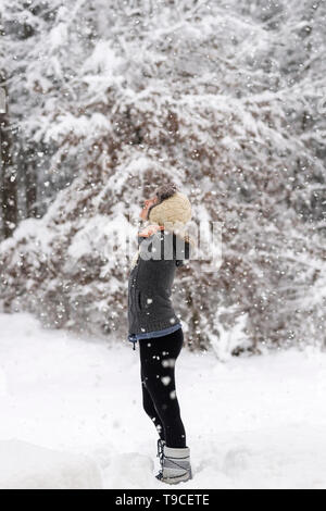 Femme debout au milieu d'une forêt enneigée Flocons accueillant et célébrer la vie avec ses bras se propager largement. Banque D'Images