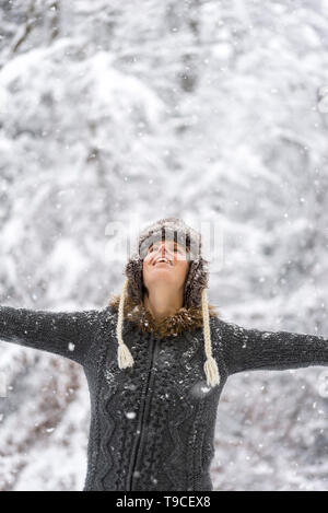 Jeune femme célébrer l'hiver avec ses bras largement propagée à la recherche vers le ciel alors que les doux flocons de neige tombent sur elle. Banque D'Images