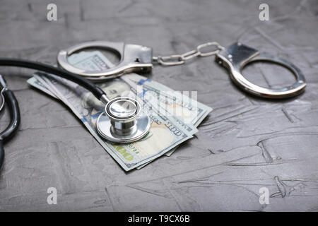 Stéthoscope avec billets de dollar et des menottes sur la table gris. Concept de la corruption Banque D'Images