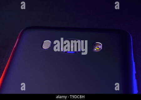Un fragment de la téléphone cellulaire cas en noir avec rétro-éclairage bleu et rouge. Le bord supérieur du téléphone se trouve sur la surface de la technologique noir appareil photo Banque D'Images