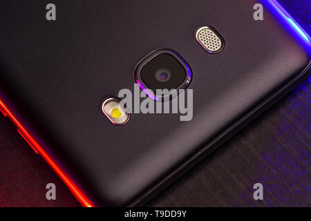 Un fragment de la téléphone cellulaire cas en noir avec rétro-éclairage bleu et rouge. Le téléphone se trouve sur la surface noire de l'appareil technologique avec un bleu Banque D'Images