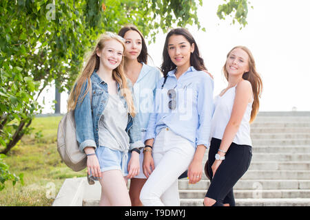 Belle drôle quatre amies se réjouissent et sourire à l'appareil photo dans le parc en été. Les jeunes femmes sont heureux Banque D'Images