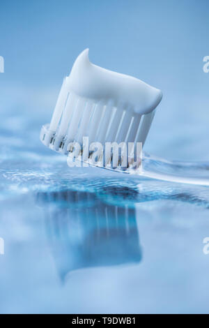 Brosse à dents en plastique transparent avec du dentifrice blanc sur un fond blanc bleu avec la réflexion sur le verre. Banque D'Images