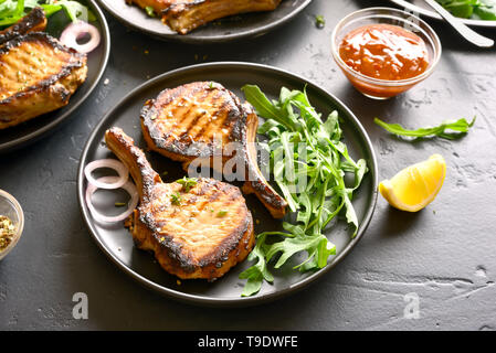 De savoureux steaks de porc grillé avec des feuilles de rukola sur table en pierre sombre Banque D'Images