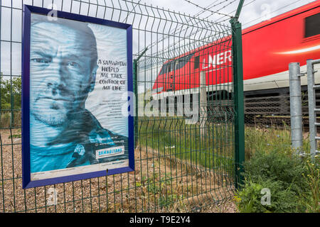 Samaritains poster 'un Samaritain m'a aidé à prendre le contrôle de ma vie' à un passage à niveau sur le chemin de fer de ligne principale de la côte est. Banque D'Images