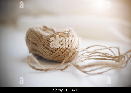 Une bobine de corde de chanvre grossier beige allongé sur un fond blanc et illuminé par la lumière du soleil. Banque D'Images