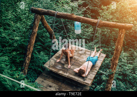 Un beau couple au repos dans la nature dans l'été, mensonge et bronzer au soleil sur une balançoire en bois. Billet, Spa, l'été, l'amour et les relations concepts Banque D'Images