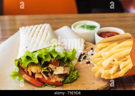 Shawarma avec la viande de poulet et frites dans une boîte sur une table dans un café. Burrito sur une planche en bois avec gros sel, poivre et de la sauce. Banque D'Images