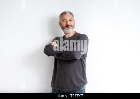Portrait de mi-longueur d'un homme barbu aux cheveux gris dans un t-shirt gris sur fond blanc. Banque D'Images